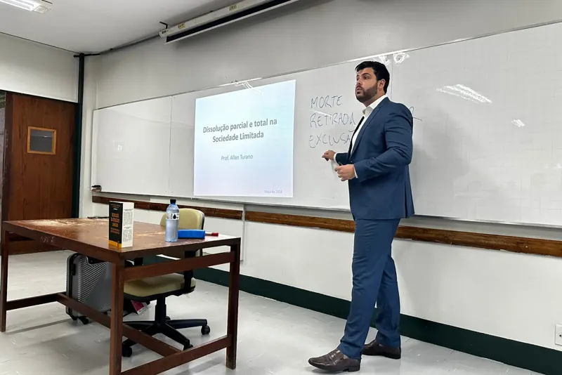 Allan Turano em sala de aula, ao lado de um slide sobre dissolução parcial e total na sociedade limitada