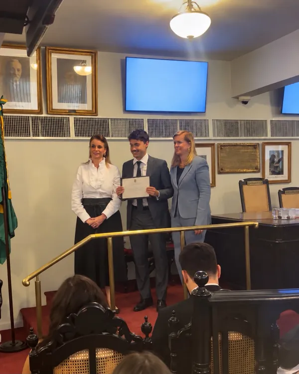 Entrega de certificado em uma cerimônia, com a bandeira do Brasil ao fundo